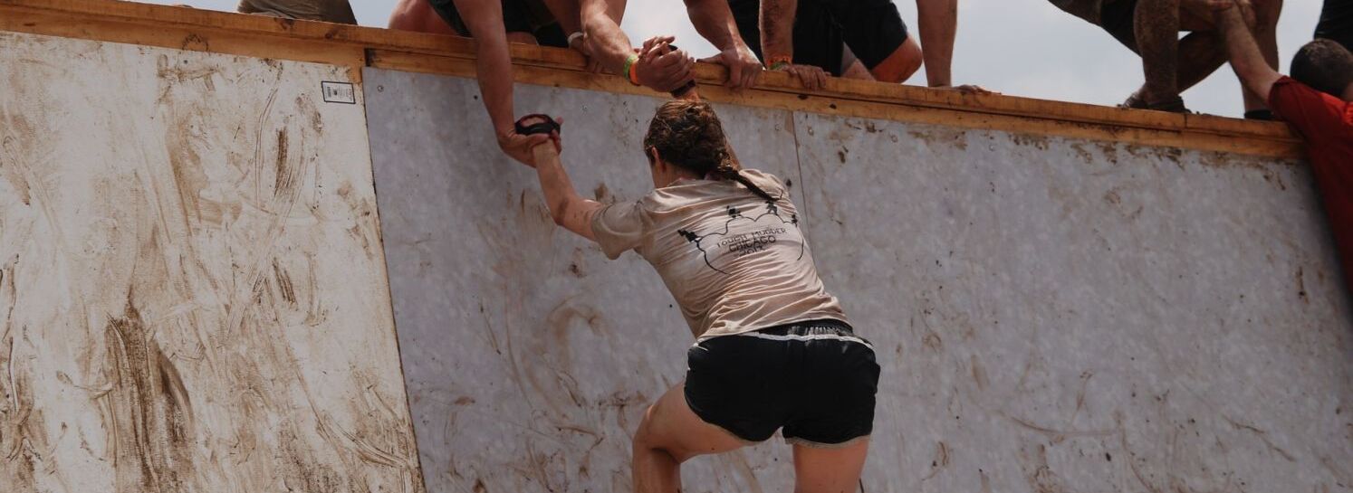 Frau wird von 2 Männern die eine Mauer hinaufgezogen